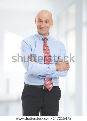 Portrait of successful businessman standing with arms crossed at office.