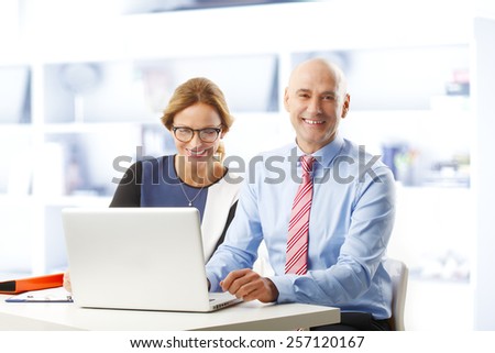 Business woman and businessman sitting at desk in front of laptop at office while analyzing financial data.