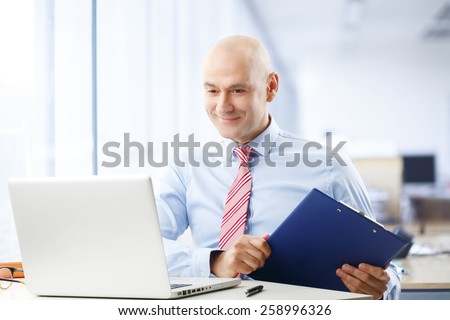 Portrait of busy broker sitting at stock exchange in front of computer while holding file in his hand. Businessman working at office.