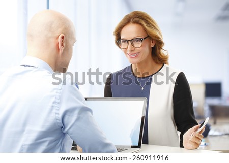 Executive businessman giving advise to business woman while working with laptop at office.