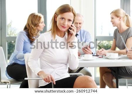 Portrait of middle age business woman sitting at meeting while making a call. Business team.
