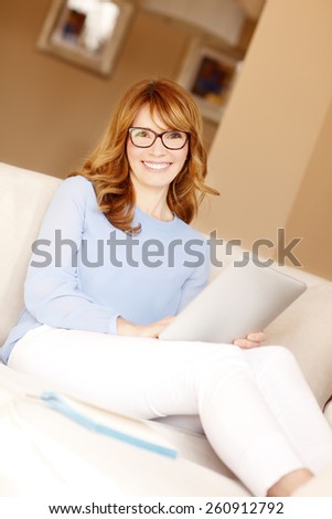 Portrait of attractive mature business woman holding digital tablet while sitting at sofa and working at home.