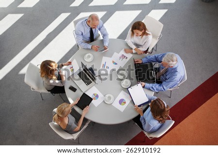 High angle view of business people discussing in a meeting while sitting at conference table. Using digital tablet and computer while analyzing financial data.  Shot taken from directly above.