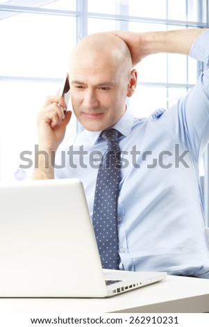 Portrait of sales man working at office while reading business report on laptop while making a call on mobile phone