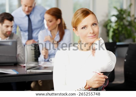 Portrait of executive business woman sitting at office while her financial team working at background with laptop. Teamwork at office.