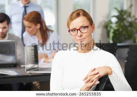 Portrait of executive business woman sitting at office while her financial team working at background with laptop. Teamwork at office.