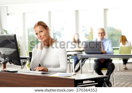 Portrait of attractive businesswoman sitting at office in front of computer and writing her presentation. Confident businesswoman looking at camera while turn around.