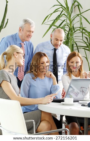 Group of businesswomen and businessmen sitting around conference table and working on presentation at laptop. Teamwork at office.