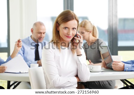 Portrait of executive businesswoman making call while sitting at meeting. Sales team sitting at background and working on presentation. Teamwork at office.