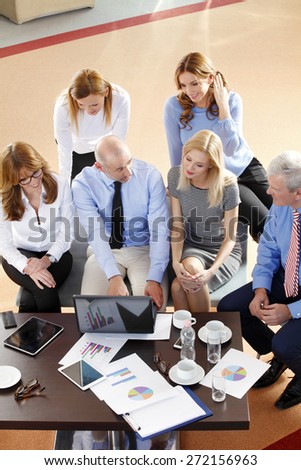 High angle view of financial business people sitting at meeting. Businesswomen and businessmen sitting at desk in front of computer and consulting from financial investment. Teamwork at office.