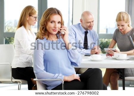 Sales team working at seminar. Portrait of attractive mature businesswoman sitting at office and making call while business people working at background.