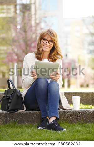 Image of businesswoman in front of an office building have a break.Typing text on her digital tablet.