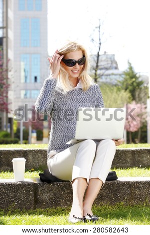 Image of attractive sales woman sitting at green area while using his laptop and surfing on internet. Business people portrait.