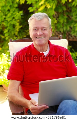 Portrait of senior businessman sitting at home in the garden and working on laptop.