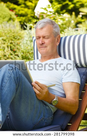 Portrait of active retired man sitting at garden and surfing on net.