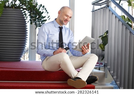 Sales man sitting at staircase while reading on digital tablet and holding his handy.