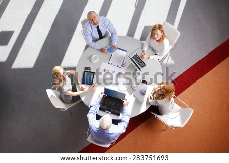 High angle view of business people discussing in a meeting while sitting at conference table. Using digital tablet and computer while analyzing financial data.  Shot taken from directly above table.