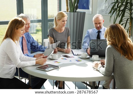 Portrait of businesswomen and businessmen sitting around conference table and consulting. Business people working with digital tablet and laptop.