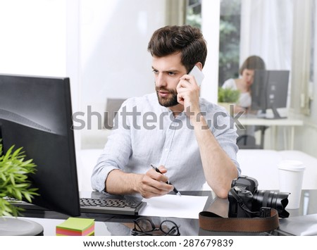 Portrait of young sales man making call while sitting at office and working online with computer.