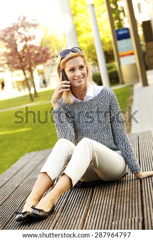 Portrait of attractive businesswoman sitting at office park and making call.