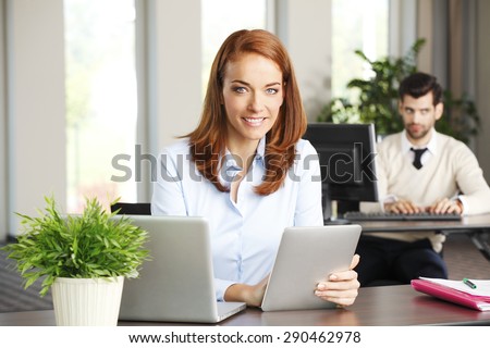 Portrait of efficiency sales woman sitting at office behind her laptop and holding hands digital tablet. Businesswoman touching the screen of tablet.