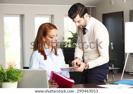 Portrait of young businessman holding hand digital tablet and consulting with executive businesswoman while sitting at office in front of laptop. Business team analyzing financial data.