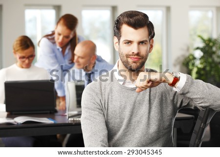 Portrait of young broker sitting at office and looking at camera. Financial experts working at computer at background.