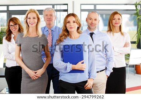 Portrait of group of business people in a row. Businesswomen and businessmen standing at office. Focus is on the woman in front.