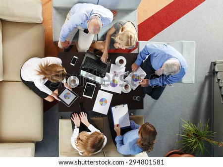 High angle view of business team in a meeting. Businesswomen and businessmen sitting around conference table and working with laptop and digital tablet analyzing diagrams.