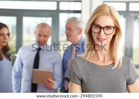 Portrait of middle age businesswoman standing in foreground while business people standing behind her. Business persons using digital tablet and consulting. Teamwork at office.