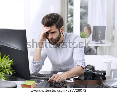 Portrait of worried young businessman sitting in front of computer at office.