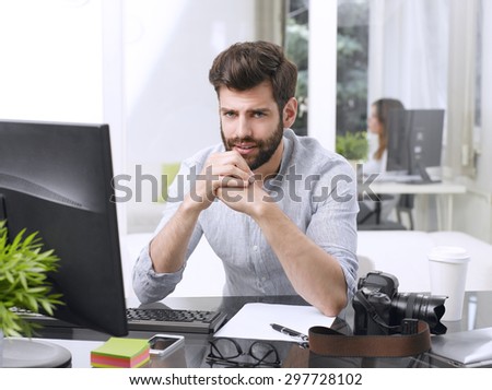 Portrait of worried young graphic studio owner sitting in front of computer at office.