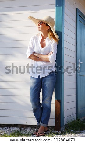 Full length portrait of smiling woman standing in front of her home. Dreamy female looking away and relaxing.