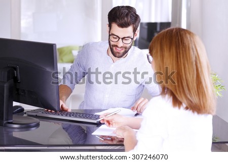 Portrait of young insurance agent sitting in front of computer and consulting with managing director.