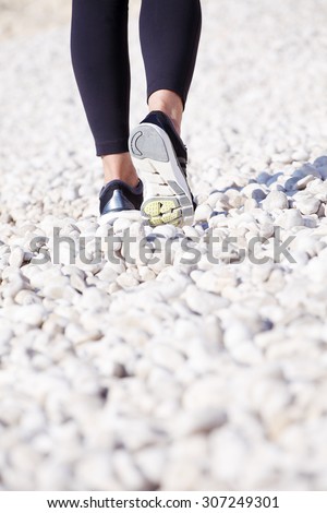 Close-up of a women\'s leg. Woman after morning run walking on beach while wearing running shoe.