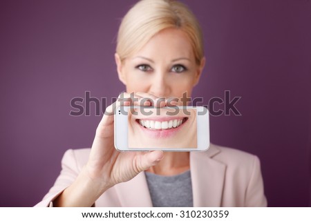 Portrait of smiling businesswoman holding hand mobile phone in front of her mouth.