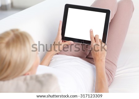 Portrait of beautiful woman sitting  back to back at sofa in living room and using digital tablet with blank screen.