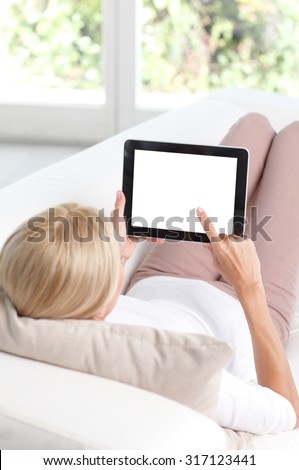 Portrait of beautiful woman sitting  back to back at sofa in living room and using digital tablet with isolated screen.