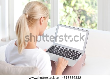 Portrait of middle age woman using her blank screen laptop while sitting back to back on the sofa at home.