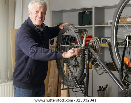 Portrait of senior man repairing bike while standing at his bike shop. Small business.