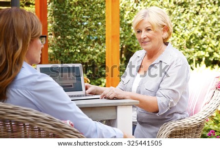 Portrait of life insurance agent consulting with retired woman while sitting at home in the garden in front of laptop.