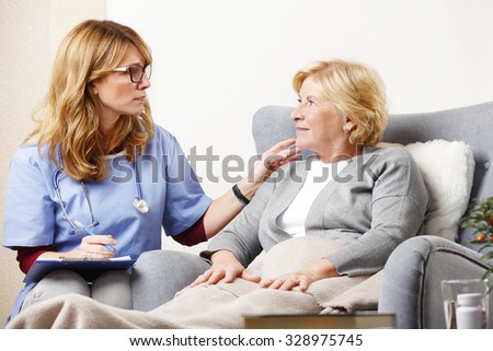 Portrait of senior woman sitting at home and consulting with middle age caregiver. Home healthcare nurse holding in her hand clipboard and giving advise while talking to elderly patient.