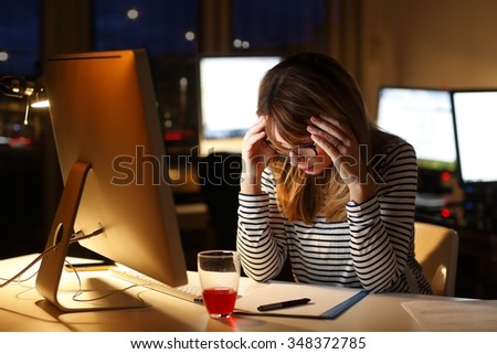Portrait of tired middle age businesswoman sitting at office desk and working late in front of a computer.