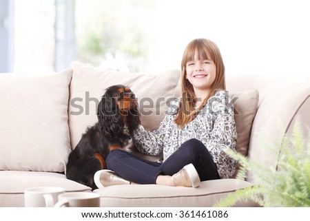 Portrait of cute little girl sitting with her pet on sofa at home.