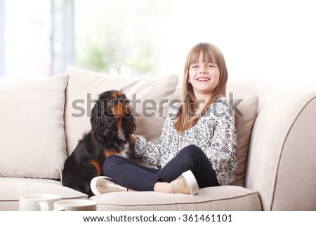 Portrait of cute little girl sitting with her pet on sofa at home and caressing her.