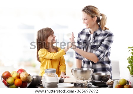 Portrait of adorable little girl and her mother baking together at home. Happy mom giving high five to her cutie daughter.