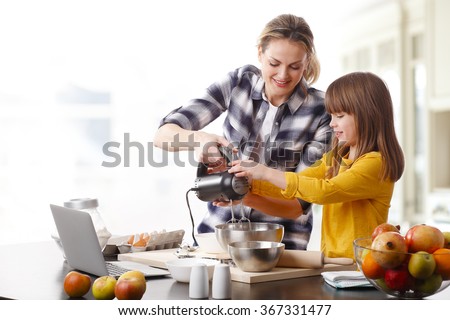 Portrait of adorable little girl and her mother baking together at home. Happy mom and her cutie daughter using kitchen robot while mixing the ingredients.