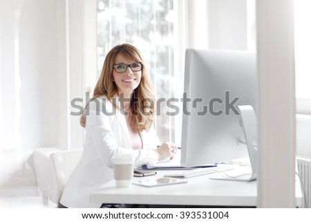 Portrait of smiling businesswoman looking at camera and smiling while working at office in front of computer.