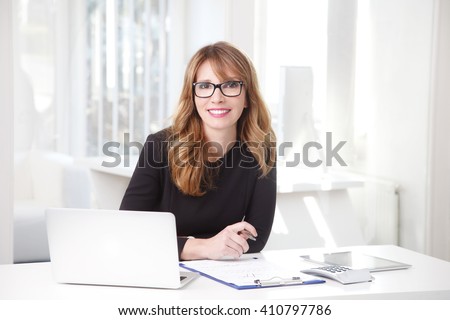 Portrait of an professional investment advisor businesswoman sitting in front of laptop at her desk in an office while looking at camera and smiling.