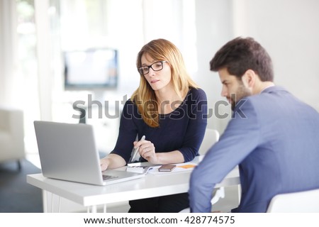 Portrait of investment advisor businesswoman sitting at office in front of computer and consulting with young professional man.